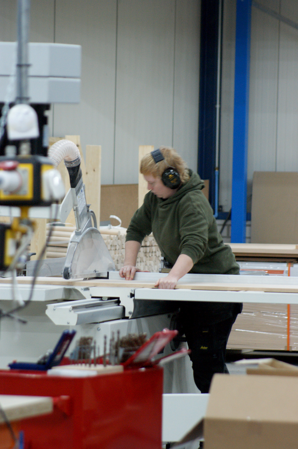 Vrouw met gehoorbescherming zaagt hout aan een CNC machine.